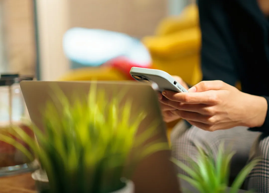 Person searching online on smartphone and laptop in a modern home with warm lighting