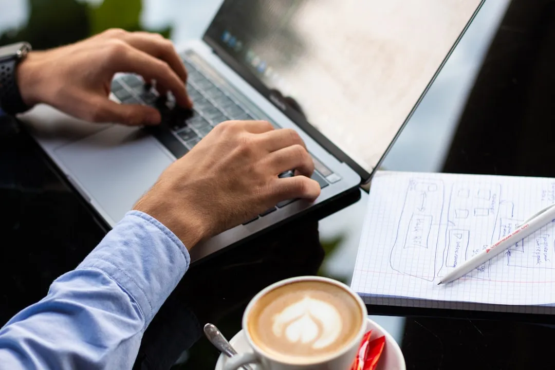 Person researching business acquisition with laptop, coffee, and notes at a professional desk